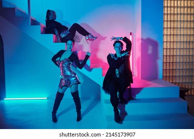 Young Teenage Couple Of Vogue Dancers In Posh Attire Performing Against Girl In Glamorous Apparel Sitting On Staircase In Modern Studio