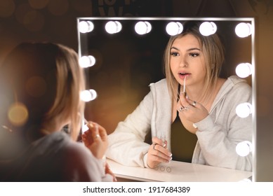 Young Teenage Girl Applying Lip Gloss In Front Of Vanity Mirror With Lights