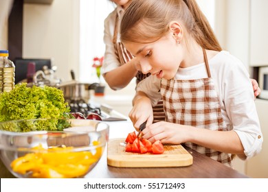 Young teenage girl cooking together with her family in the kitchen. Cute girl chopping tomatoes for salad