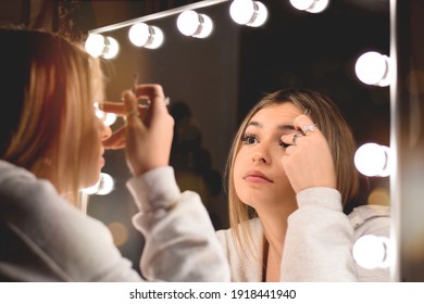 Young Teenage Girl Doing Make Up In Front Of Vanity Mirror With Lights