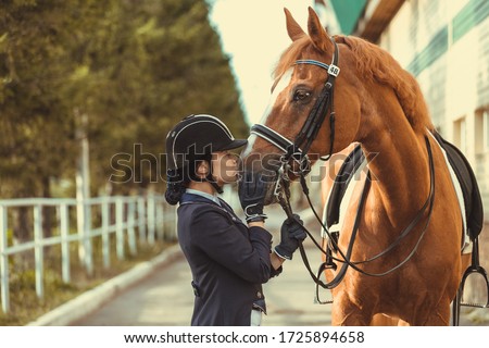 Young teenage girl equestrian kissing her favorite red horse. Multicolored outdoors horizontal image. Dressage outfit 