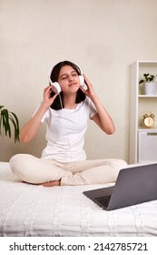 A Young Teenage Girl With Headphones Listening To Music While Sitting On The Bed. The Girl Enjoys Music With Her Eyes Closed. Vertical Orientation. Mock Up.