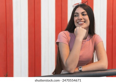 Young teenage girl leaning on a railing next to a beach hut, looking smiling towards the beach. - Powered by Shutterstock