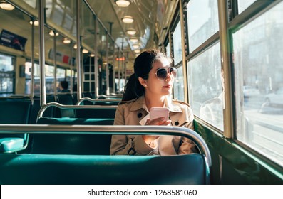 Young teenage girl using her cell phone in public transportation while commuting. asian woman in sunglasses looking view outside the bus window. empty streetcar cable car in san francisco.