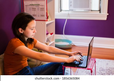 Young teenage girl using laptop. Homeschooling, hands on keyboard in bedroom.