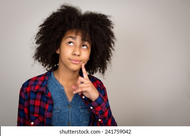 Young Teenage Girl With Wacky Afro Hair Looking Up Thinking And Solving Problems Isolated Against A Grey Background.