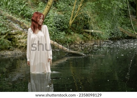 A young teenage girl in a white dress stands in the water, in a lake against a background of green foliage. day Ivan bathed.