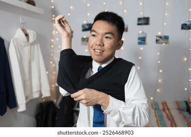 A young teenage male student is dressing up for school at home in his bedroom, putting on a vest sweater that is part of his school uniform - Powered by Shutterstock