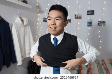 A young teenage male student is dressing up for school at home in his bedroom, putting on a vest sweater that is part of his school uniform - Powered by Shutterstock