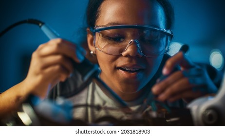 Young Teenage Multiethnic Schoolgirl is Studying Electronics and Soldering Wires and Circuit Boards in Her Science Hobby Robotics Project. Girl is Working on a Robot in Her Room. Education Concept.