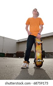 A young teenage skateboarding standing with his skateboard in an urban setting.