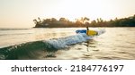 Young teenager boy with colorful surfboard go to foamy sea for surfing. He enjoying a beautiful sunset light on Dewata beach on Sri Lanka. Active sport vacation and exotic countries traveling concept.