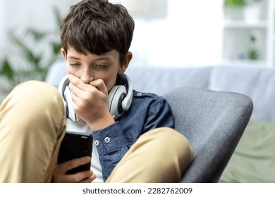 Young teenager boy reading bad news on phone, son sitting on sofa in living room with headphones at home closeup. - Shutterstock ID 2282762009