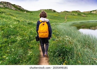 Young teenager boy with yellow backpack  walking in the high mountains in French Alps. Hiking concept. Summer activities.