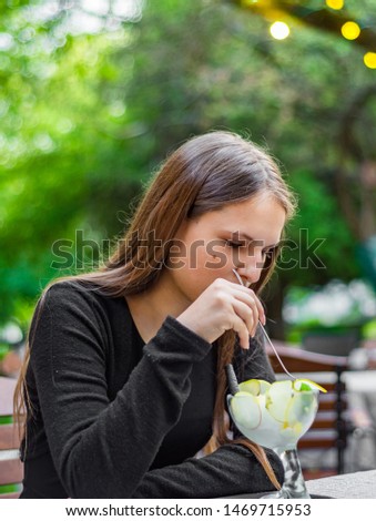 young teenager brunette girl with long hair eating ice cream in outdoor cafe