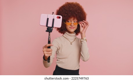 Young Teenager Child Girl Kid Blogger Taking Selfie On Smartphone Selfie Stick, Communicating Video Call Talking Online With Subscribers. Little Funny Children Isolated On Studio Pink Background