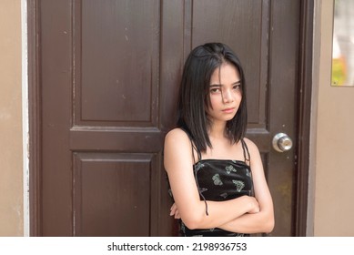A young teenager in a foul mood leaning against the main door of her house fiercely looks at the camera as she smize her eyes.