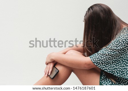 Young teenager girl hugging her knee and holding a  smartphone, Cyber bullying in kid, depressed, despair child mental illness health, fear of missing out, FOMO, social distancing