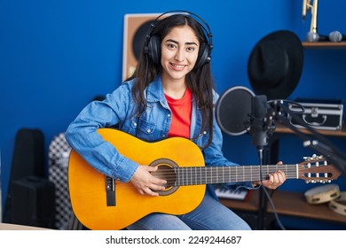 Young teenager girl playing classic guitar at music studio looking positive and happy standing and smiling with a confident smile showing teeth  - Powered by Shutterstock