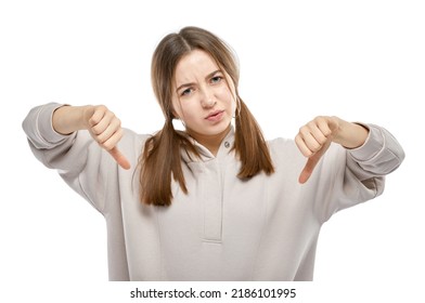 Young teenager girl showing dislike emotion with thumbs down with two hands. Disagree gesture. Studio porttrait isolated on white background.