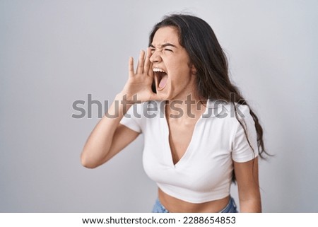 Young teenager girl standing over white background shouting and screaming loud to side with hand on mouth. communication concept. 