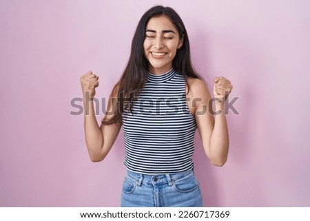 Young teenager girl wearing casual striped t shirt excited for success with arms raised and eyes closed celebrating victory smiling. winner concept. 