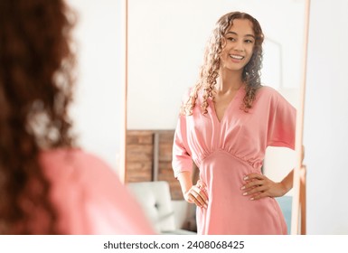 Young teenager girl wears fashionable pink dress, admiring herself in mirror indoors, looking at her reflection, reflecting happiness and confidence in new outfit, feeling beautiful and positive - Powered by Shutterstock