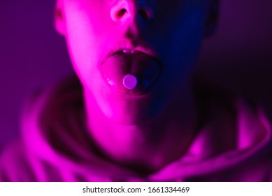 Young teenager in a pink hoodie takes a drug in pills. Tongue guy with lsd wheel