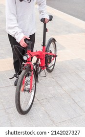 Young teenager riding his red folding bicycle on the sidewalk, heading to the city center. He is wearing comfortable clothes for pedaling. Transportation. Real people. Vertical.