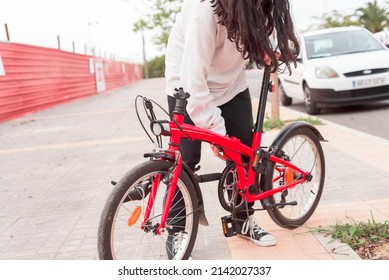 Young teenager riding his red folding bicycle on the sidewalk, heading to the city center. He is wearing comfortable clothes for pedaling. Transportation. Real people. Horizontal.