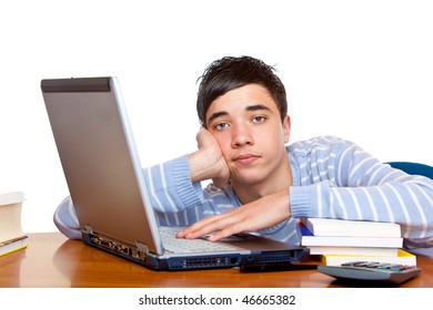 Young teenager is sitting on desk and learns with computer and books for his exams. He looks frustrated into camera. Isolated on white.