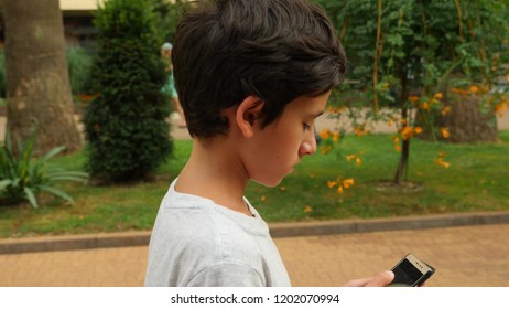 Young Teenager With Smartphone Walking In City, Slow Motion . The Boy Walks On The Street And Looks Into His Phone