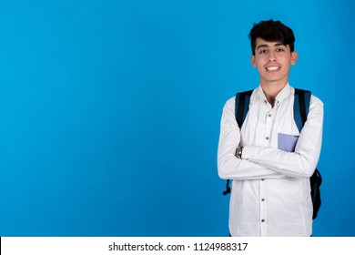 Young teenager standing on the right side of the portrait crossed arms wearing backpack on a blue background.