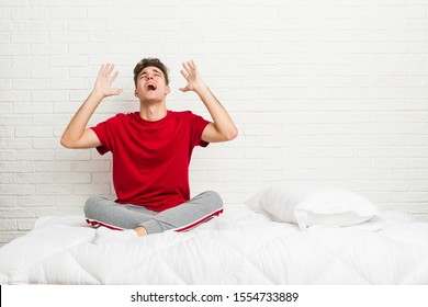 Young teenager student man on the bed screaming to the sky, looking up, frustrated. - Shutterstock ID 1554733889