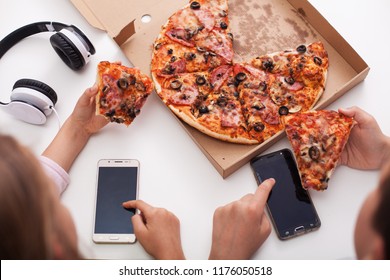 Young teenagers checking their phones while eating pizza - the urge of constant connection infiltrating everyday life - Powered by Shutterstock