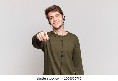 young telemarketer pointing at camera with a satisfied, confident, friendly smile, choosing you