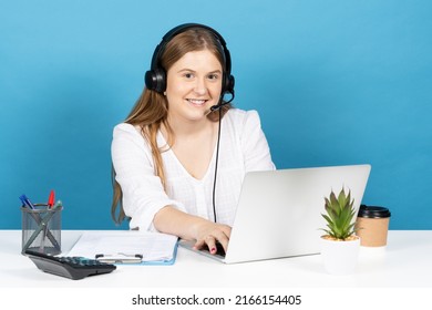 Young Telephone Or Telemarketing Operator Working On Laptop. Blonde Woman Looking At Camera Isolated On Blue Background.