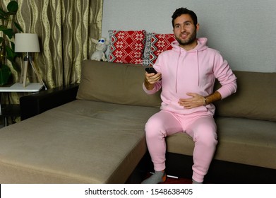 Young Television Addict Man Sitting On Sofa At Home And Watching TV Using Remote Control, Looking Excited, Pumping Out Someone Else's Comedy Comedy Movie Or Live Music At Night