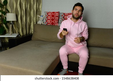 Young Television Addict Man Sitting On Sofa At Home And Watching TV Using Remote Control, Looking Excited, Pumping Out Someone Else's Comedy Comedy Movie Or Live Music At Night