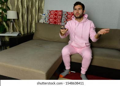 Young Television Addict Man Sitting On Sofa At Home And Watching TV Using Remote Control, Looking Excited, Pumping Out Someone Else's Comedy Comedy Movie Or Live Music At Night