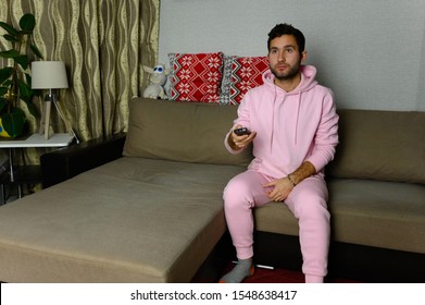 Young Television Addict Man Sitting On Sofa At Home And Watching TV Using Remote Control, Looking Excited, Pumping Out Someone Else's Comedy Comedy Movie Or Live Music At Night