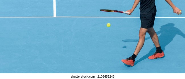 Young tennis player playing with ball and racket on blue hard tennis court during match or training. Sports active game. Tennis background, copy space - Powered by Shutterstock