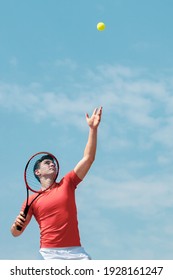 Young Tennis Player With Racket Throws The Ball Prepares To Serve At Beginning Of Game Or Match. Cute Male Tennis Player Athlete In Action. Competitive Sport. Vertical Banner Copy Space