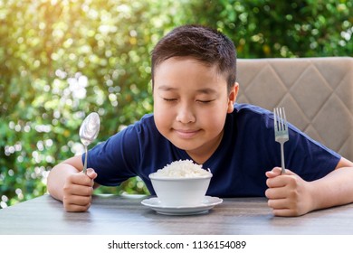 Young Thai Boy Eating Organic White Rice By Stainless Spoon On Green Bokeh Background From Tree. Rice Is A Major Consumption Of Thai People.