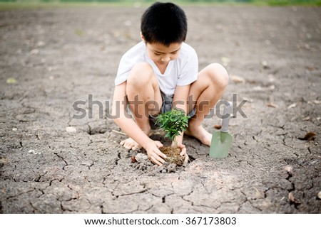 Young Thai boy planting little seedling on dry and crack empty land. Earthday concept.