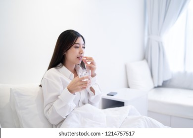 Young Thai girl Business woman taking medicine and drinking water,holding pills,glass of water on bed in hospital bedroom,she work hard while feels sick,drug remedy,health care Medical people concept