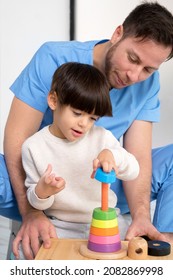Young therapist helping cute little boy who has cerebral palsy, playing with developing toy at rehabilitation clinic. High quality photo