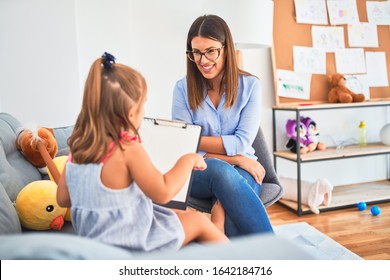 Young Therapist Woman Speaking And Treating Child, Counselor And Behaviour Correction At Pedagogue Payroom Taking Notes On Clipboard