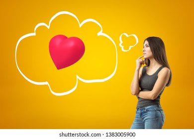 Young thinking brunette girl wearing casual jeans and t-shirt with red heart on yellow background. Casual clothing. Feelings and emotions. Gestures and body language - Shutterstock ID 1383005900