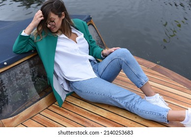 A young thinking girl on a boat. A girl in style, head bowed and legs outstretched in a position of thought. With her hand in her hair, a girl with brown hair sits on a boat and looks down.